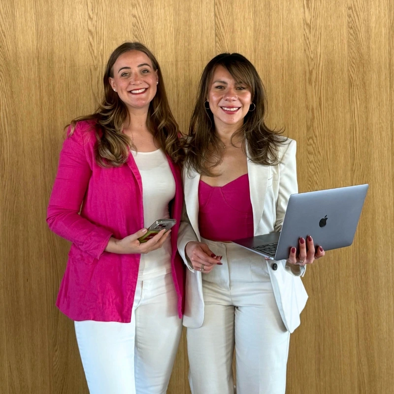 Lot & Helen in front of a wall, smiling with a phone and laptop in their hands